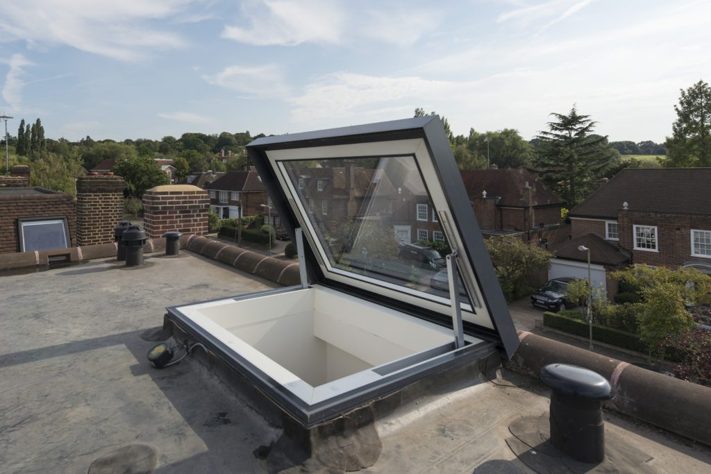 An open skylight on a flat rooftop with a view of suburban houses and greenery under a clear sky.