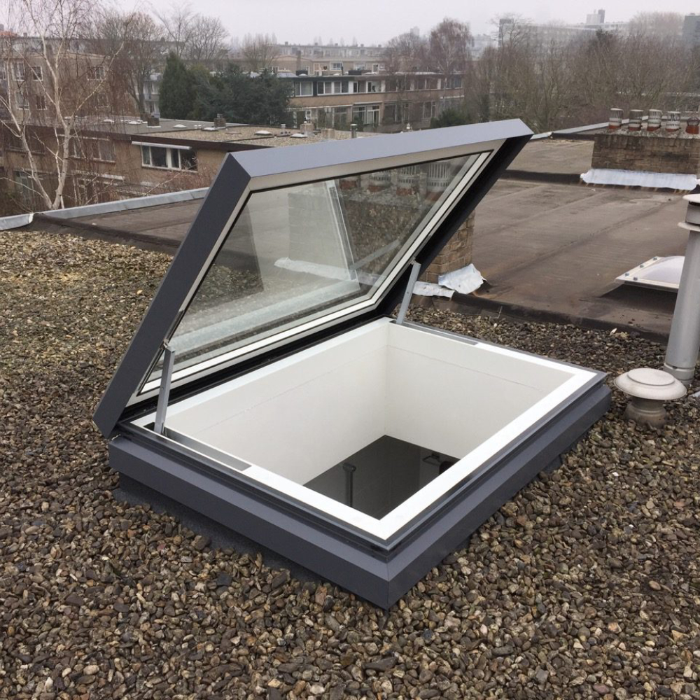Open glass roof hatch on a gravel-covered flat rooftop with a view of an urban residential area in the background.