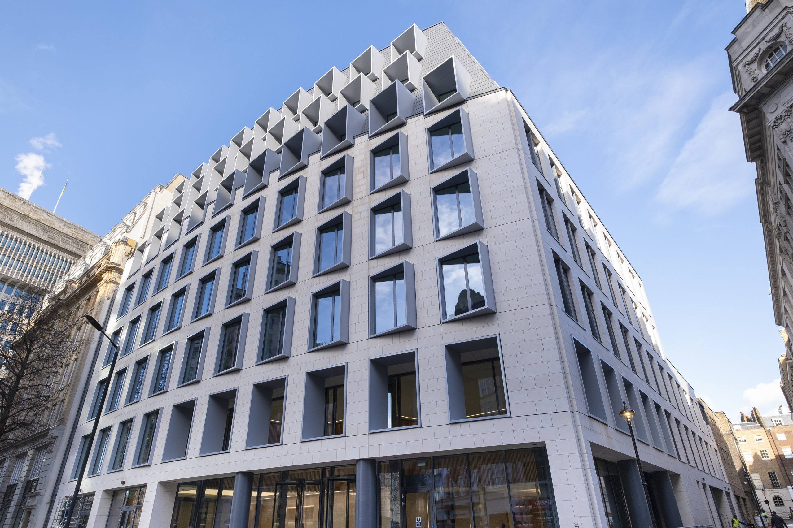 Modern office building with geometric window design, bespoke commercial rooflights, and white façade, viewed from street level against a blue sky.