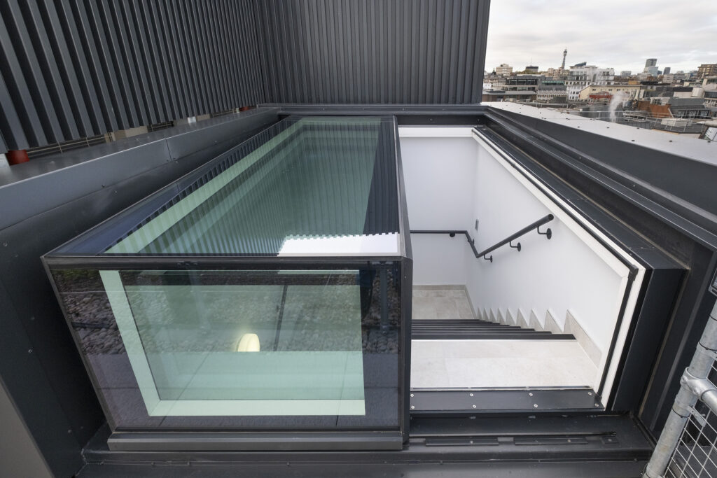 A striking three-wall box rooflight with steps leading down and a cityscape visible in the background.