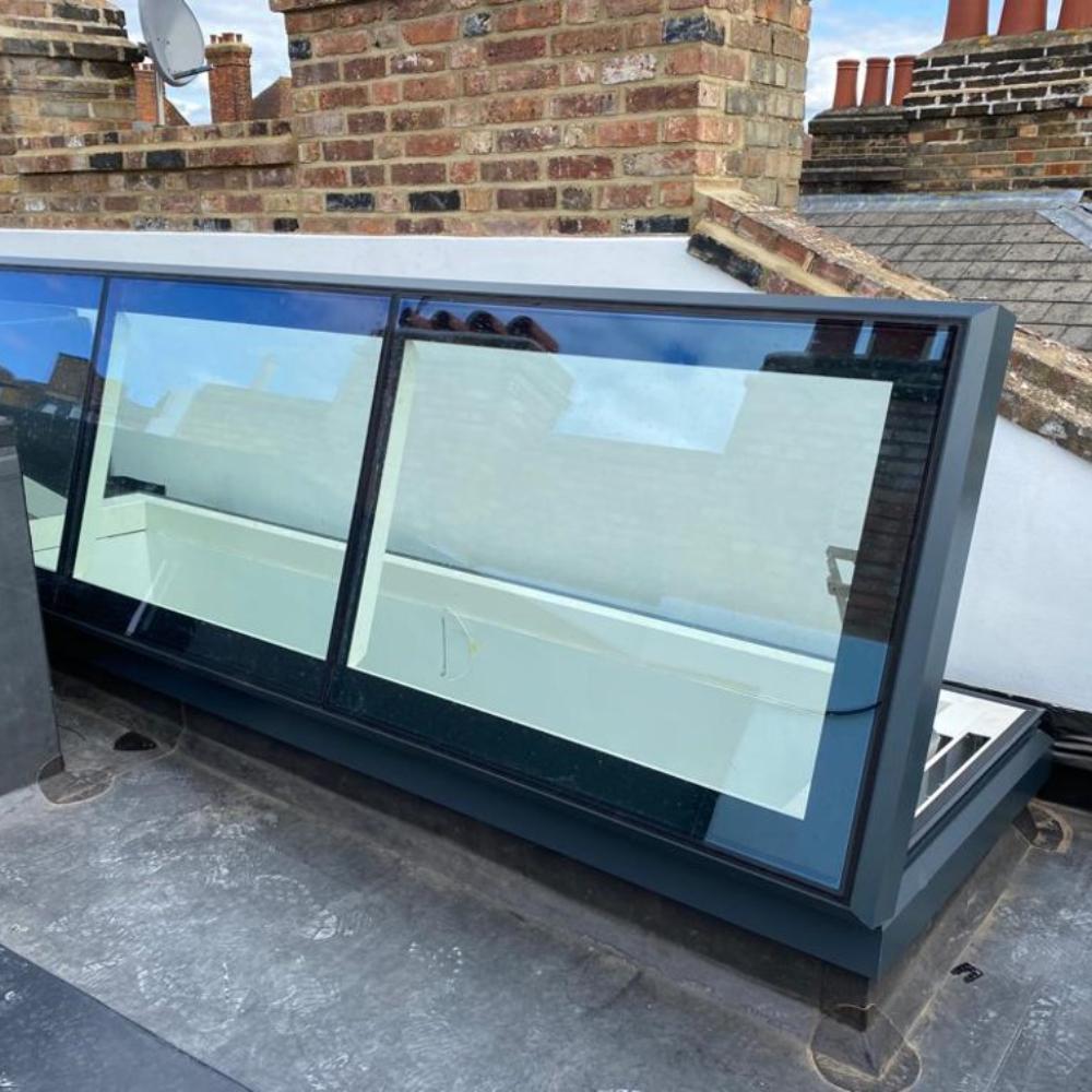 large access hatch rooflight open with side hinge A large access hatch rooflight on a flat roof, opened via side hinge black metal framed with chimneys and rooftops visible in the glass reflection.
